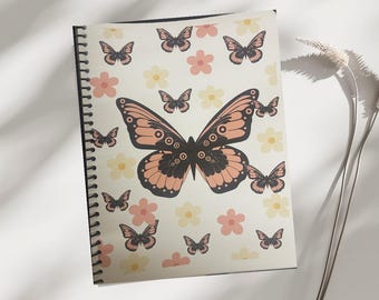 May include: A spiral-bound notebook featuring a cream-colored cover adorned with a repeating pattern of butterflies and flowers. The butterflies are in shades of peach, black, and brown, while the flowers are peach and yellow. The notebook is open, revealing the design.