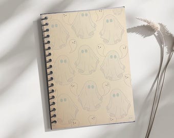 May include: A spiral-bound notebook featuring a repeating pattern of friendly ghost illustrations in light gray on a beige background. The ghosts have round, blue eyes. The notebook's spine is black.