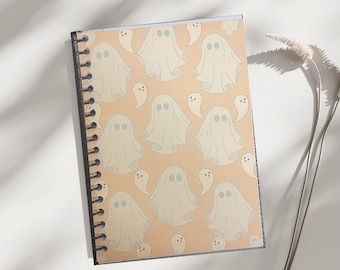 May include: A spiral-bound notebook featuring a repeating pattern of friendly ghost illustrations on a peach background. The ghosts are white with blue eyes. The notebook is open, displaying the patterned cover.