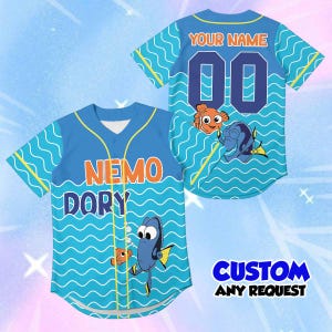 May include: A light blue baseball jersey featuring a wavy pattern, yellow piping, and cartoon fish characters. The front displays the text NEMO DORY, while the back shows the text YOUR NAME and the number 00. The text CUSTOM ANY REQUEST is visible.