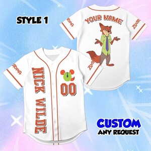 May include: A white baseball jersey with orange trim featuring the text NICK WILDE and the number 00 on the front. The back displays a cartoon fox character, the text YOUR NAME, and the word Zootopia on the sleeves. Text reads STYLE 1.