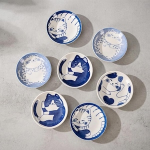 May include: A set of seven round ceramic plates featuring various blue and white cat illustrations. Each plate displays a different feline pose, including striped, spotted, and solid blue patterns, all with smiling expressions and curled tails.
