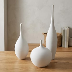 Peut inclure: Trois vases en céramique blanche avec une surface texturée à rainures horizontales. La collection comprend un vase haut et élancé, un vase de taille moyenne avec un col allongé et un vase plus court et arrondi avec une ouverture étroite.