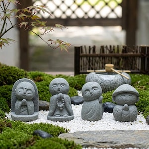 Puede incluir: Cuatro pequeñas estatuas de piedra gris de figuras sonrientes en varias posturas, incluyendo dos con las manos juntas en oración, una sosteniendo cuentas de oración y una con sombrero, sobre un lecho de grava blanca y musgo verde.