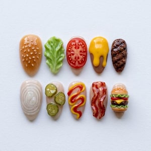 May include: A collection of ten uniquely designed nail art pieces, each resembling a component of a hamburger. The designs include a sesame seed bun, lettuce, tomato, cheese, a burger patty, onion, pickles, mustard, bacon, and a miniature burger.