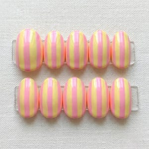 May include: A set of ten oval-shaped press-on nails arranged in two rows of five. Each nail features a glossy finish with vertical stripes alternating between pastel yellow and soft pink colors, displayed on two clear adhesive strips.