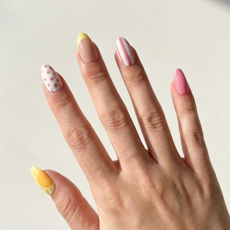 K&ouml;nnte beinhalten: Mandelformige Fingern&auml;gel mit verschiedenen Nageldesigns. Der Daumen zeigt ein gelbes Sonnenmotiv, der Zeigefinger hat rosa Punkte, der Mittelfinger eine gelbe French-Spitze, der Ringfinger rosa Streifen und der kleine Finger ist einfarbig rosa.