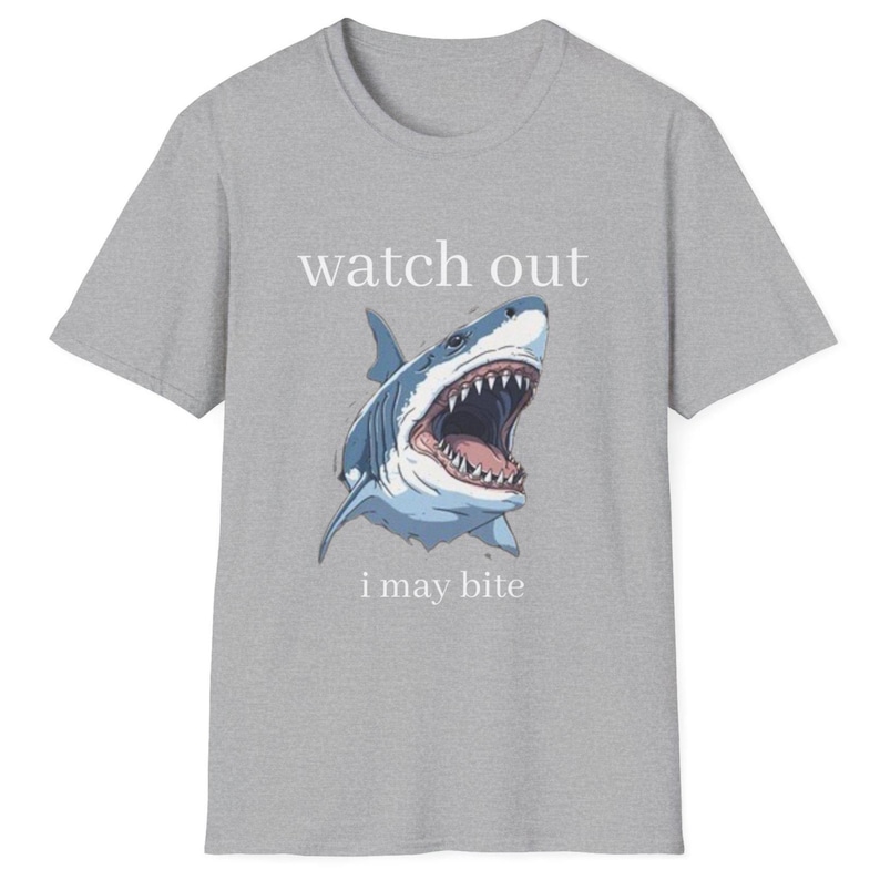 May include: A gray t-shirt featuring a shark illustration with an open mouth, displaying sharp teeth. The text "watch out" is above the shark, and "i may bite" is below. The shark is blue and white.