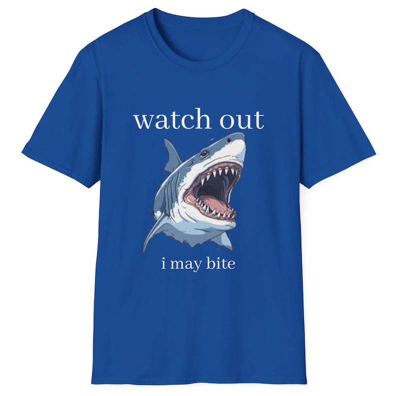 May include: Royal blue t-shirt featuring a detailed illustration of a shark with an open mouth, teeth visible. The text "watch out" is above the shark, and "i may bite" is below.