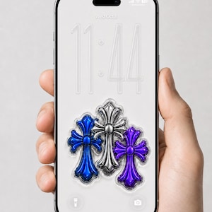 May include: A smartphone screen shows a wallpaper with three decorative crosses in blue, silver, and purple. The phone is held in a hand, with the time 11:44 and the date Wednesday, October 8 displayed on the screen.