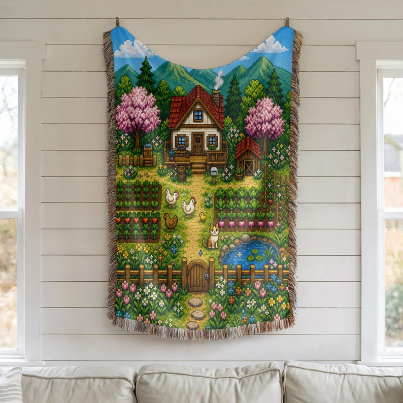 May include: A tapestry depicting a pixelated countryside scene with a house, garden, pond, and animals. The blanket has a blue sky border and fringed edges. The scene includes a house with a red roof, trees, and a path leading to a wooden gate.