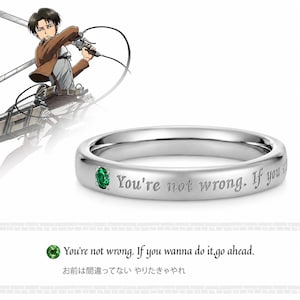 Könnte beinhalten: Ein silberfarbener Metallring mit einem kleinen, runden, grünen Edelstein, der in das Band eingelassen ist. Die Außenfläche des Rings ist mit dem Text "You're not wrong. If you wanna do it, go ahead." graviert. Eine Anime-Charakterillustration ist zu sehen.