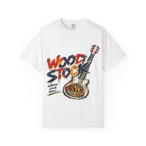 May include: A white short-sleeve t-shirt featuring a graphic of an electric guitar and the text "WOODSTOCK" in a distressed, multi-coloured font. Below the guitar, the text reads "where rock lives..." and "NYC" is printed on the guitar body.