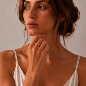 Può includere: Un anello in oro caratterizzato da una fascia con una serie di piccole perle sferiche disposte in fila. L'anello ha una finitura metallica lucida ed è indossato su un dito. Il design consiste in una fascia continua di sfere dorate uniformi.