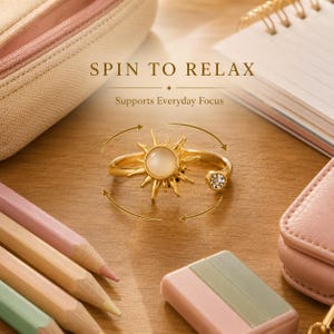 Op de afbeelding: Een goudkleurige ring met een zonvormig middendeel met een centrale opake steen en een kleine heldere kristal aan één uiteinde van de open ring. De tekst SPIN TO RELAX en Supports Everyday Focus is zichtbaar boven de ring met pijlen.