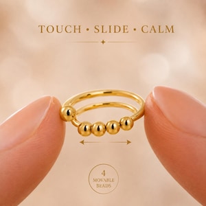 Puede incluir: Un anillo de tono dorado que presenta cuatro pequeñas cuentas esféricas móviles a lo largo de la banda. El texto TOUCH • SLIDE • CALM está impreso sobre el anillo, y el texto 4 MOVABLE BEADS está impreso debajo, junto a una flecha.