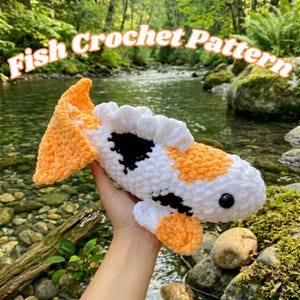 May include: A handmade crochet fish in white, orange, and black. The fish has a fluffy texture and a black eye. The text "Fish Crochet Pattern" is displayed in the image.