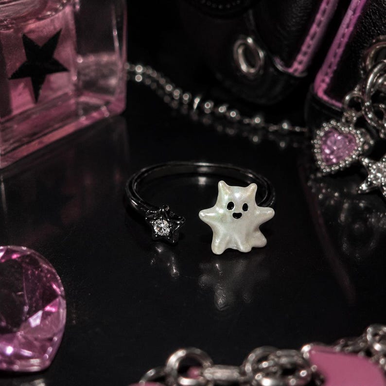 Puede incluir: Un anillo abierto negro que presenta un dije blanco nacarado con forma de fantasma en un extremo y un peque&ntilde;o cristal transparente con forma de estrella engastado en metal negro en el otro. El dije de fantasma tiene dos puntos negros por ojos.