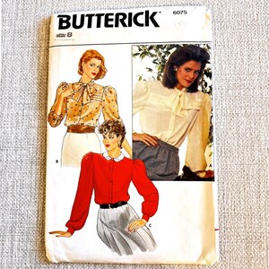 May include: A Butterick 6075 size 8 sewing pattern envelope featuring illustrations of three blouse styles. One blouse is beige with colorful polka dots and a bow tie, one is solid cream with a bow tie, and one is solid red with a white collar.