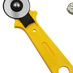May include: A yellow rotary cutter with a circular silver blade and a black centre hub. The handle features a recessed grip area and a circular hole at the base for hanging. A logo in the top right corner displays the text Craft Verse ART & ETC.