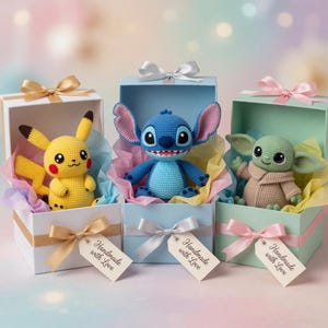Op de afbeelding: Drie handgemaakte gehaakte karakterpoppen: Pikachu, Stitch en Grogu, elk genesteld in een geschenkdoos met vloeipapier en een lint. De dozen zijn wit, lichtblauw en groen, met labels "Handmade with Love".