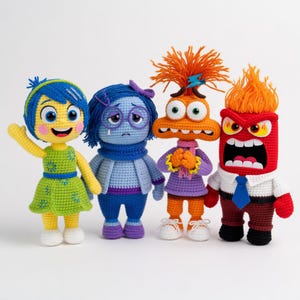 Puede incluir: Cuatro muñecos de ganchillo hechos a mano que representan personajes de la película animada "Del revés". Los muñecos presentan colores vibrantes: amarillo, verde, azul, morado, naranja y rojo. Cada muñeco tiene expresiones faciales y ropa únicas.