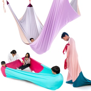 May include: A collection of sensory swing hammocks and body socks made from stretchy fabric. The hammocks feature lavender, light grey, and peach tones, while the body socks display vibrant combinations of teal, pink, and magenta with red straps.