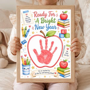 May include: A framed print titled Ready For A Bright New Year featuring a large red handprint inside an apple outline. The design includes colorful illustrations of crayons, stacked books, alphabet blocks, and notes with text You Can Do Amazing Things and Be Kind Be You.