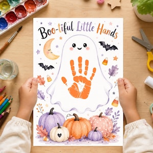May include: A white paper sheet featuring the text Boo-tiful Little Hands, a central orange handprint inside a ghost outline, a crescent moon, bats, candy corn, and colourful pumpkins in shades of purple, orange, and pink on a wooden surface.