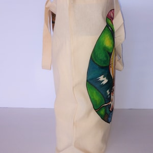 May include: A beige canvas tote bag with a colorful graphic design of a bird on the side. The bag has two long handles.