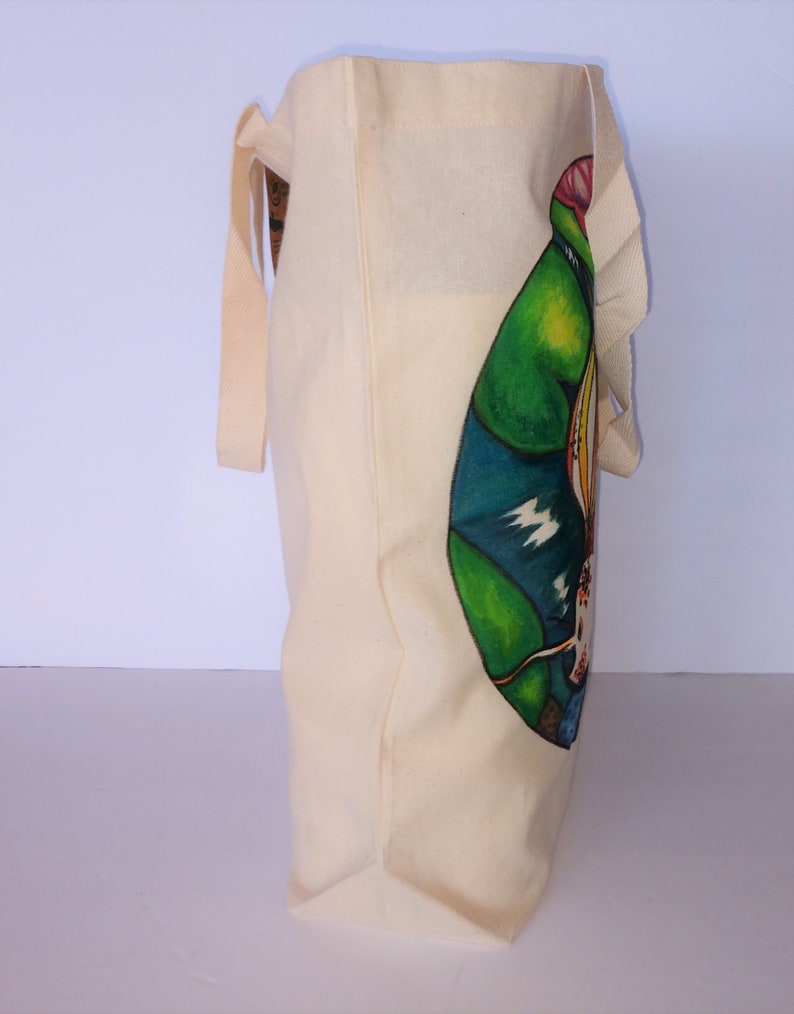 May include: A beige canvas tote bag with a colorful graphic design of a bird on the side. The bag has two long handles.