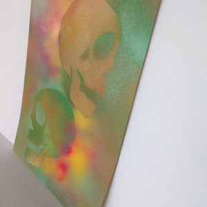May include: Two green and gold skulls are painted on a textured canvas background with a colorful spray paint effect.