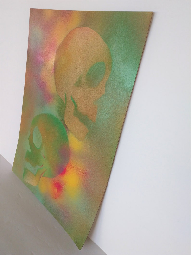 May include: Two green and gold skulls are painted on a textured canvas background with a colorful spray paint effect.