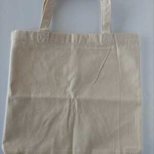 May include: A plain, off-white canvas tote bag with two fabric handles.