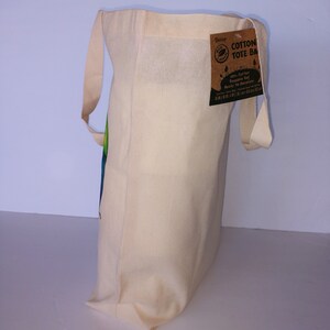 May include: A natural cotton tote bag with a brown paper tag that reads "Cotton Tote Bag 100% Cotton Reusable Bag Ready To Decorate".