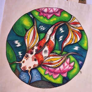 May include: A white tote bag with a colorful hand-painted design of a koi fish swimming in a pond with lily pads. The fish is red, orange, yellow, and white with black spots. The lily pads are green with pink flowers.