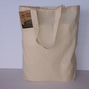 May include: A natural-colored cotton tote bag with a brown label that reads "Eco Cotton Tote Bag, 100% Cotton, Reusable Bag, Ready to Decorate, Carry Your Style, 10 oz, 14x16", and a green leaf logo.