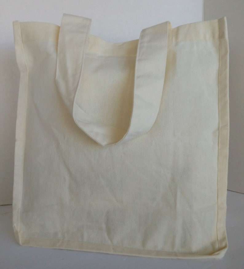 May include: A plain white canvas tote bag with two handles. The bag is made of a soft, natural fabric and has a simple, classic design.