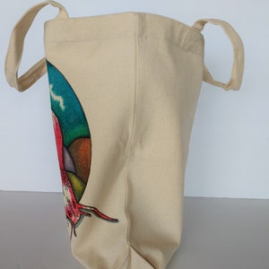 May include: A beige canvas tote bag with a colorful graphic of a lobster on the front. The bag has two long handles.