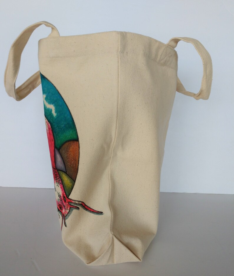 May include: A beige canvas tote bag with a colorful graphic of a lobster on the front. The bag has two long handles.