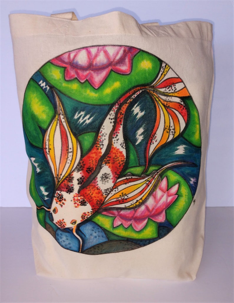 May include: A white canvas tote bag with a colorful hand-painted design of a koi fish swimming among pink and green water lilies. The fish has red, orange, yellow, black, and white scales.