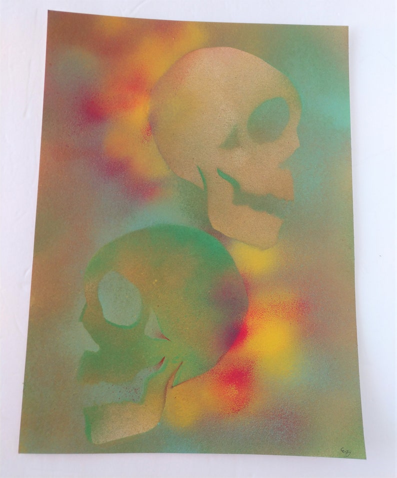 May include: Two skulls painted in a spray paint technique on a canvas background. The top skull is painted in gold and the bottom skull is painted in green. The background is a mix of yellow, red, and blue.