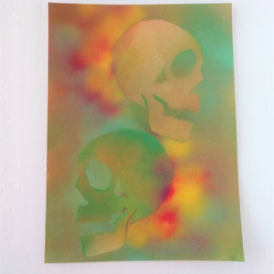 May include: Two skulls are painted in green and gold on a background of yellow, orange, red, and blue spray paint.