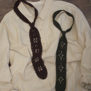 May include: Two crochet neckties, one in dark brown and one in dark green, featuring a repeating openwork floral pattern throughout the length of the ties. The ties are displayed against a cream-colored button-down shirt with long sleeves.