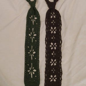 May include: Two crocheted neckties, one in dark green and one in dark brown. Each tie features a repeating openwork floral pattern running down the center, with a solid crocheted knot section at the top and a rounded bottom edge for both items.