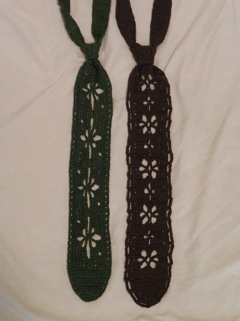 May include: Two crocheted neckties, one in dark green and one in dark brown. Each tie features a repeating openwork floral pattern running down the center, with a solid crocheted knot section at the top and a rounded bottom edge for both items.