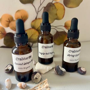 May include: Three amber glass dropper bottles with black caps and white labels. The labels read Crabiverse, with text identifying the contents as Coconut Salmon Oil, Pumpkin Bell Pepper, and Shrimp Squid Oil, all marked as 100% Organic.