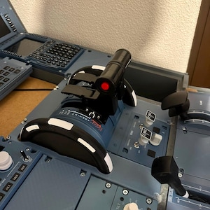 Può includere: Un quadrante della manetta di un aereo blu con leve nere con accenti bianchi, una maniglia centrale nera con una luce circolare rossa e vari interruttori a levetta etichettati ENG 1, ENG 2 e INTEG LT. Il pannello di controllo include vari quadranti.