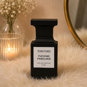 May include: A matte black rectangular perfume bottle with a square cap. The white label features the black text TOM FORD, FUCKING FABULOUS, EAU DE PARFUM, and 50 ML. The bottle has a distinct architectural shape with a wide top and base.