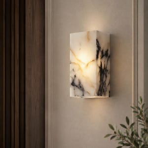 May include: A rectangular wall sconce featuring a polished white stone surface with prominent black and gold veining. The fixture emits a warm, soft glow from within, highlighting the natural translucent patterns and textures of the stone material.